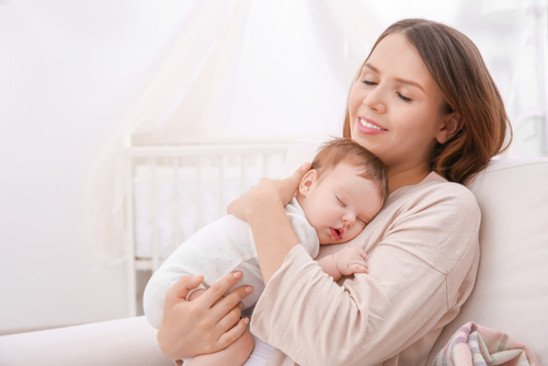 Young,Mother,Holding,Sleeping,Baby,At,Home